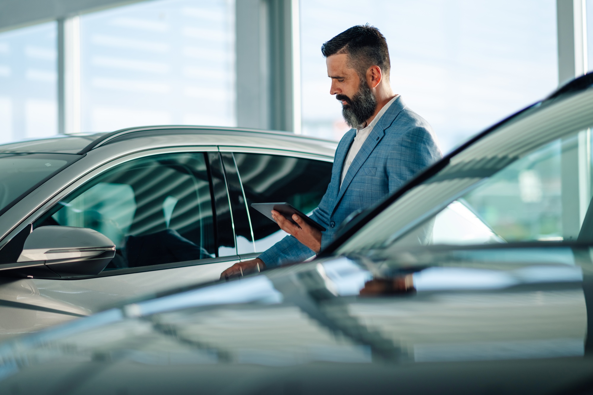 Man in suit at car dealership reviewing vehicle details on tablet.