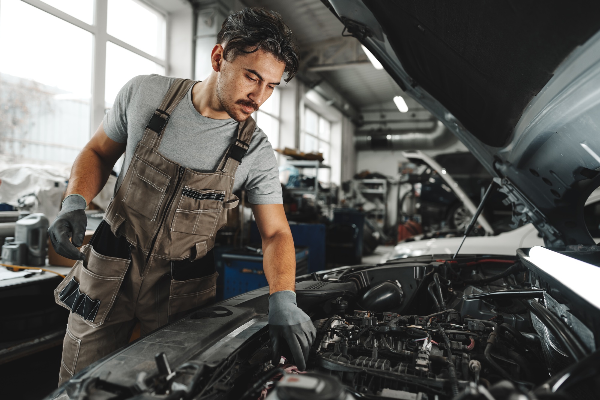 Young male mechanic examining engine under hood of car at the repair garage