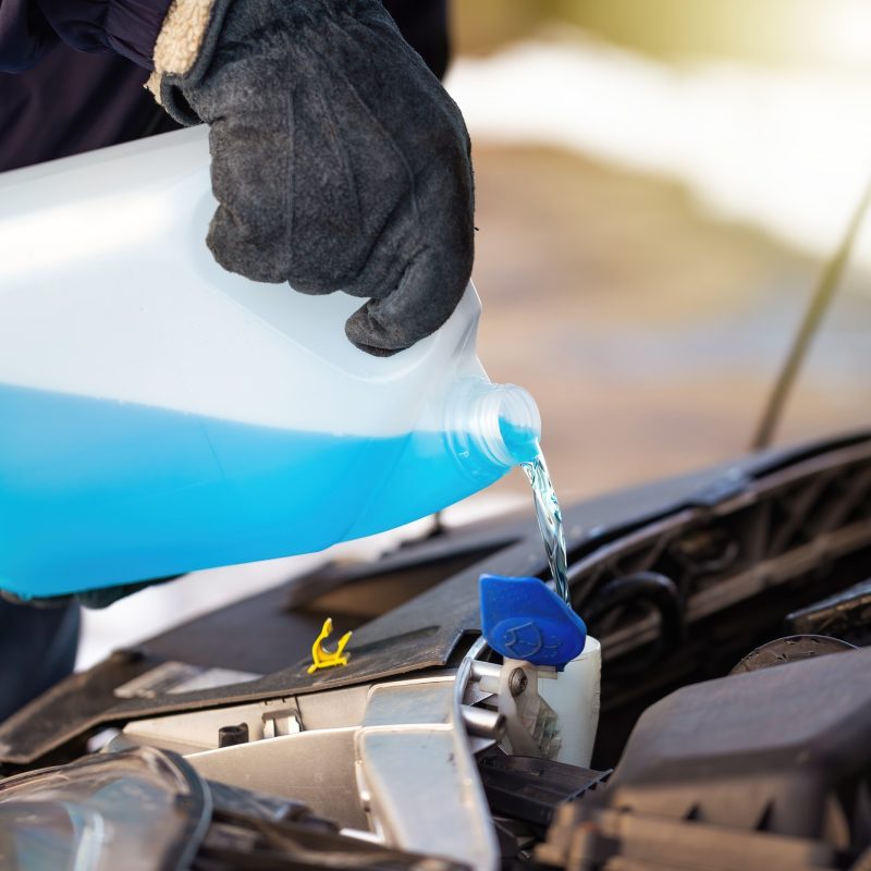 Man filling antifreeze coolant for cleaning front window with snow in background